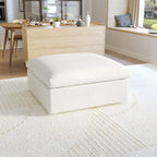 A white, down-filled comfort storage ottoman, placed in a bright living room setting.