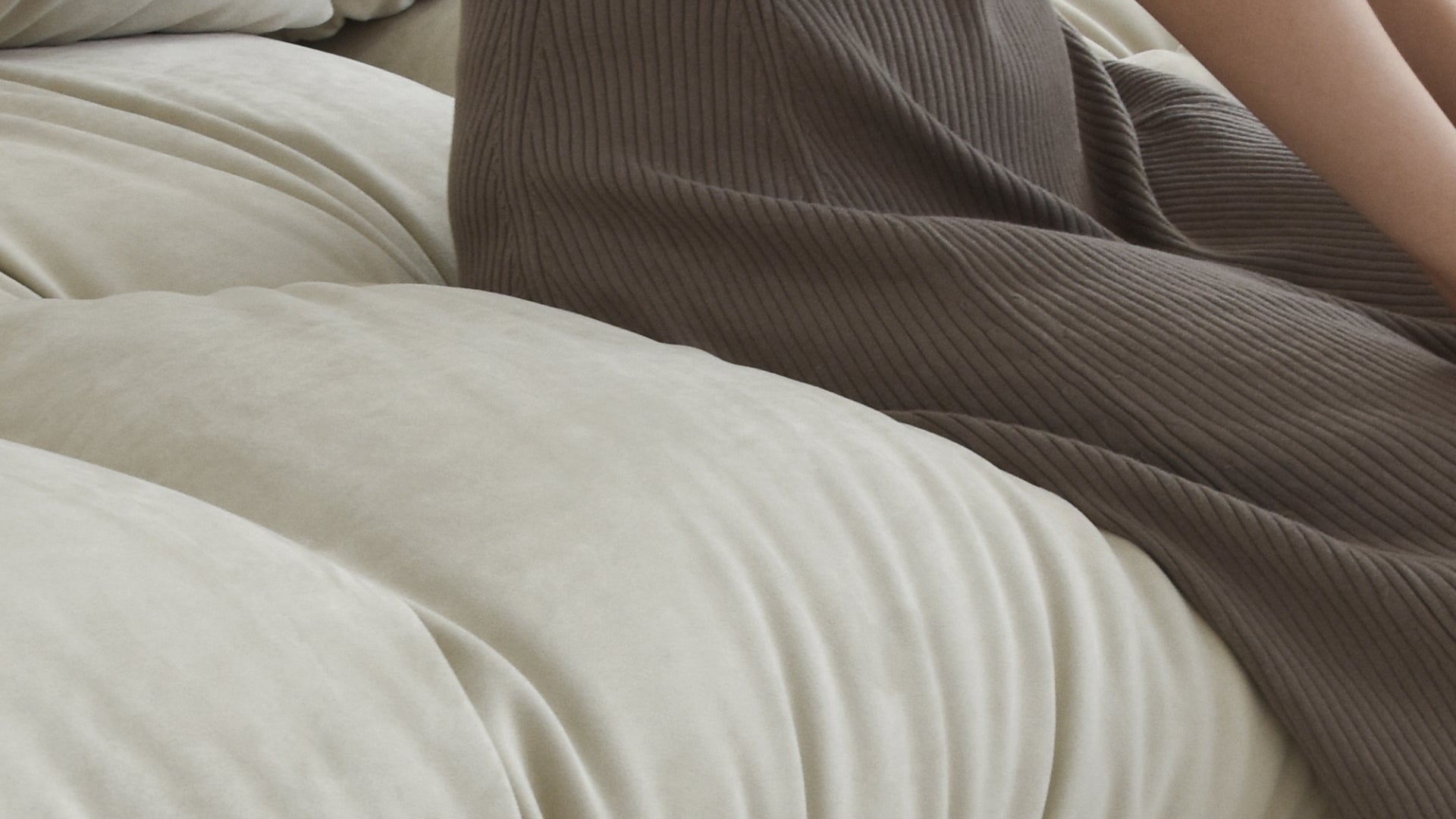 Person sitting on a beige suede sofa to show its softness