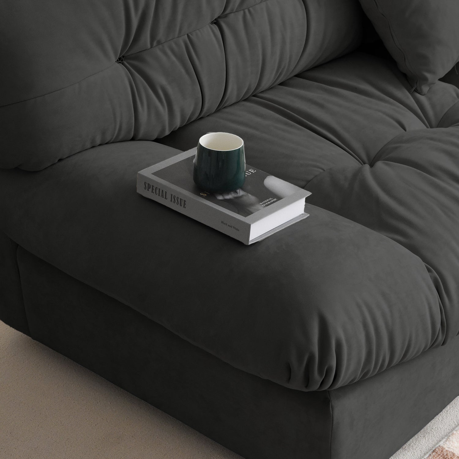 Close-up of a wide armrest of a gray suede sofa with book and a cup standing on it.
