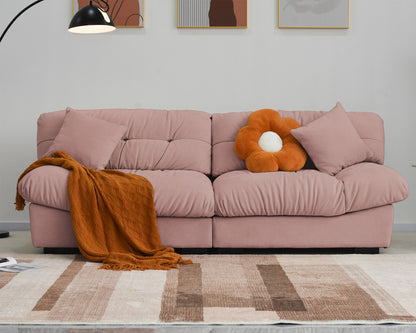 An 89-inch pink microfiber suede sofa with orange decor, featuring a solid hardwood frame, presented in a cold lightning in a living room setting with minimalistic decor, including an art print on the wall.