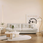 A beige microfiber suede sofa in a warm lightning with splitable seats placed in a room with minimalistic decor, including a 'Matisse' poster on the wall.