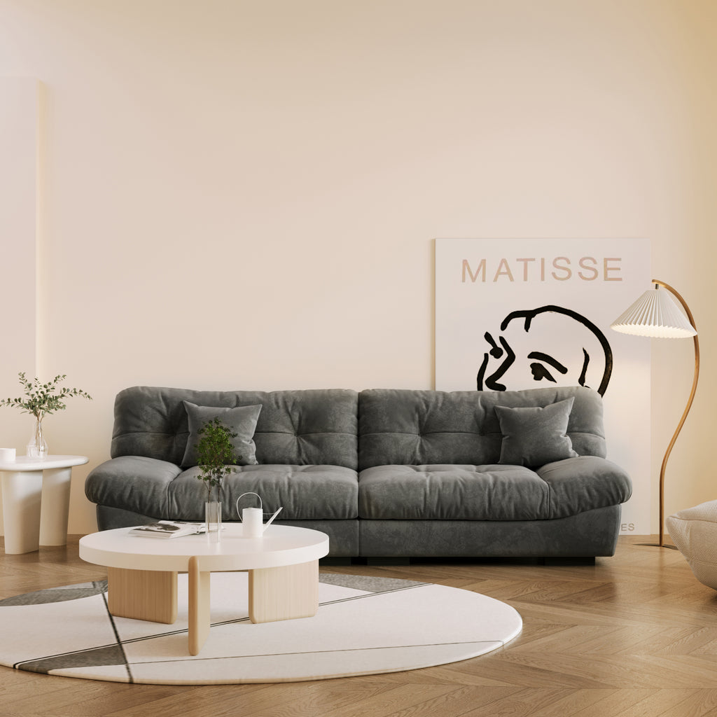 A gray microfiber suede sofa in a warm lightning with splitable seats placed in a room with minimalistic decor, including a 'Matisse' poster on the wall.