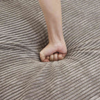 Close-up of a hand pressing on a seat cushion of a brown corduroy sofa