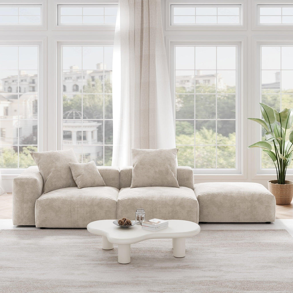 A beige corduroy 3-seat sectional lounger sofa with detachable armrests and removable covers, positioned in a bright room with large windows.
