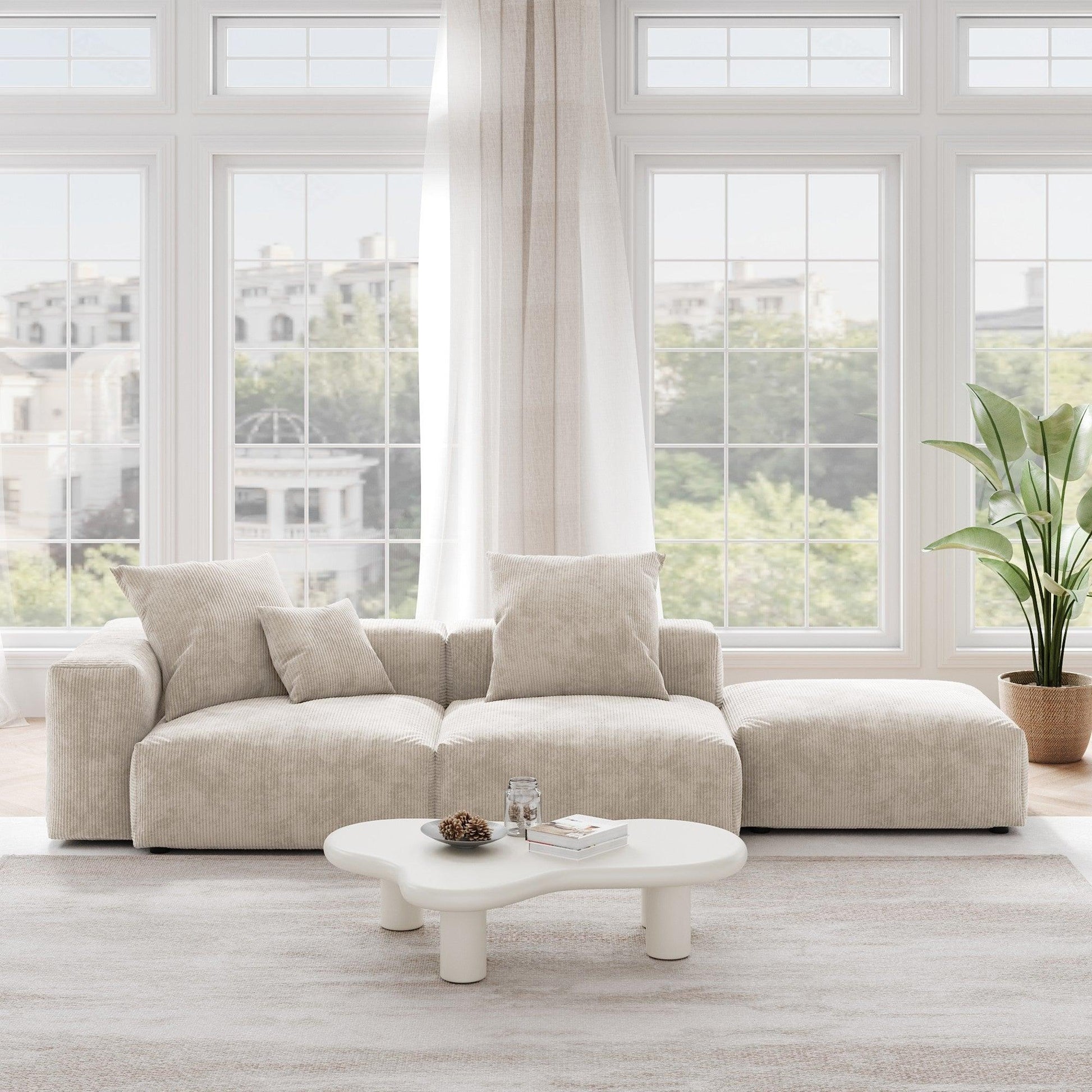 A beige corduroy 3-seat sectional lounger sofa with detachable armrests and removable covers, positioned in a bright room with large windows.