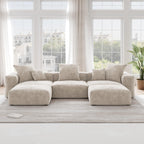 A beige corduroy U-shaped sectional modular sofa with detachable armrests and removable covers, placed in a room with large windows.