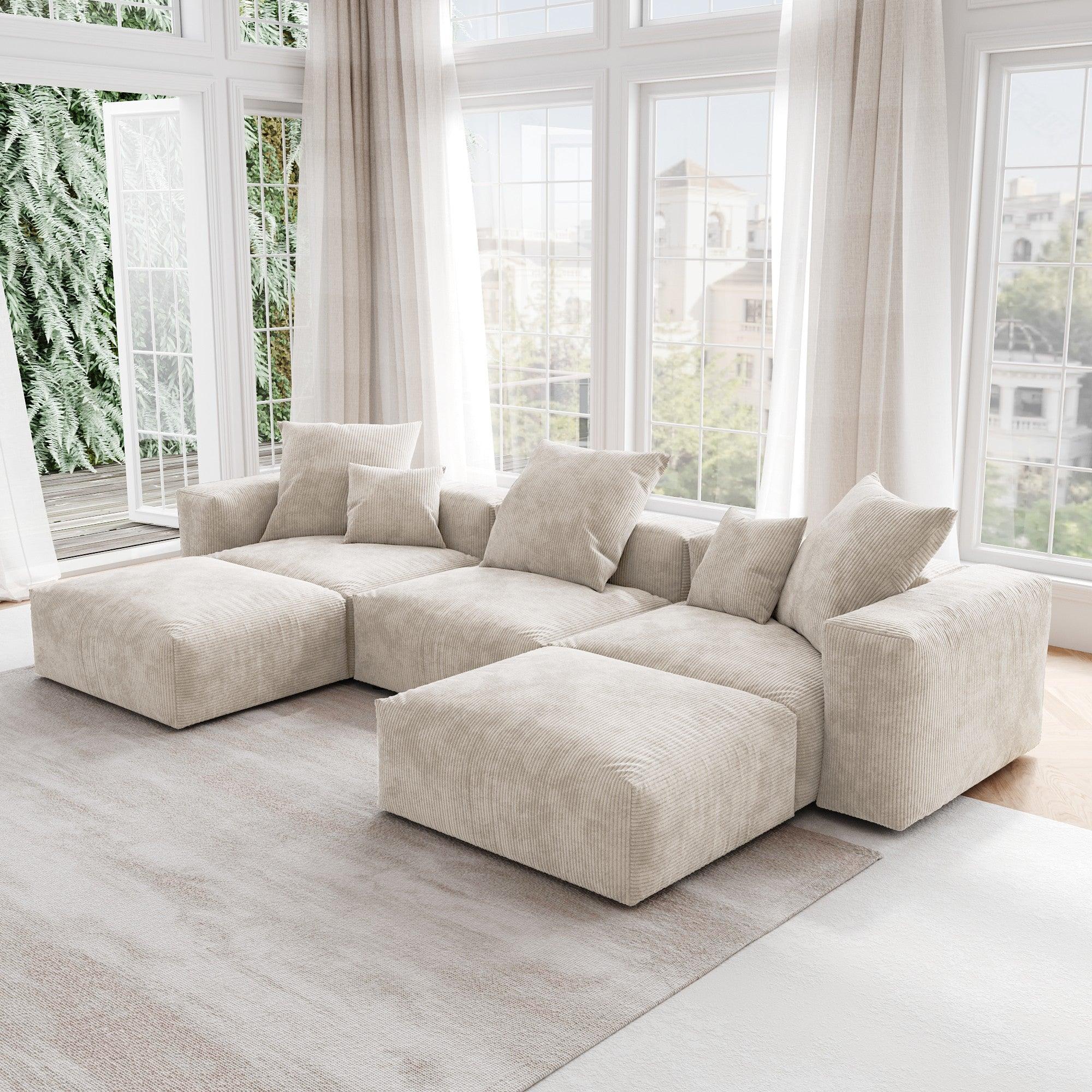 A beige corduroy U-shaped sectional modular sofa with detachable armrests and removable covers, placed in a room with large windows.