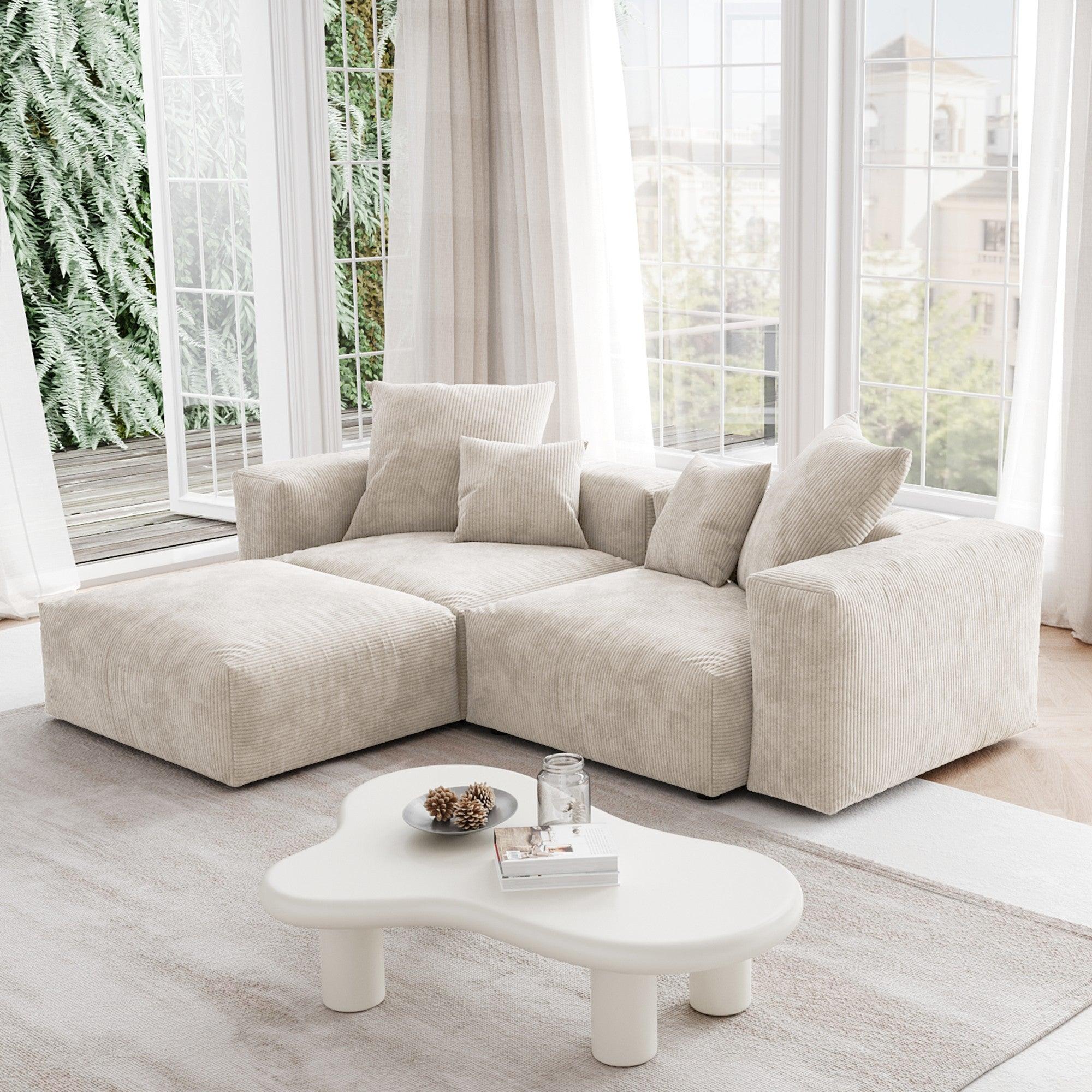 A beige corduroy sectional modular sofa with detachable armrests and removable covers, featuring a chaise lounge configuration placed in a room with large windows.