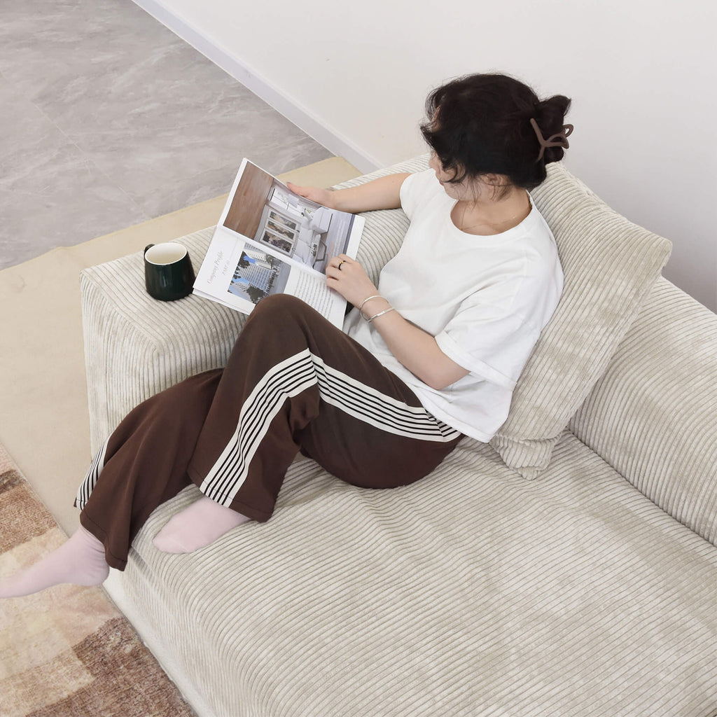 Person sitting and reading magazine on a beige corduroy sofa