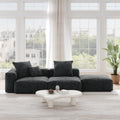 A black corduroy sectional lounger sofa with detachable armrests and removable covers, positioned in a bright room with large windows.