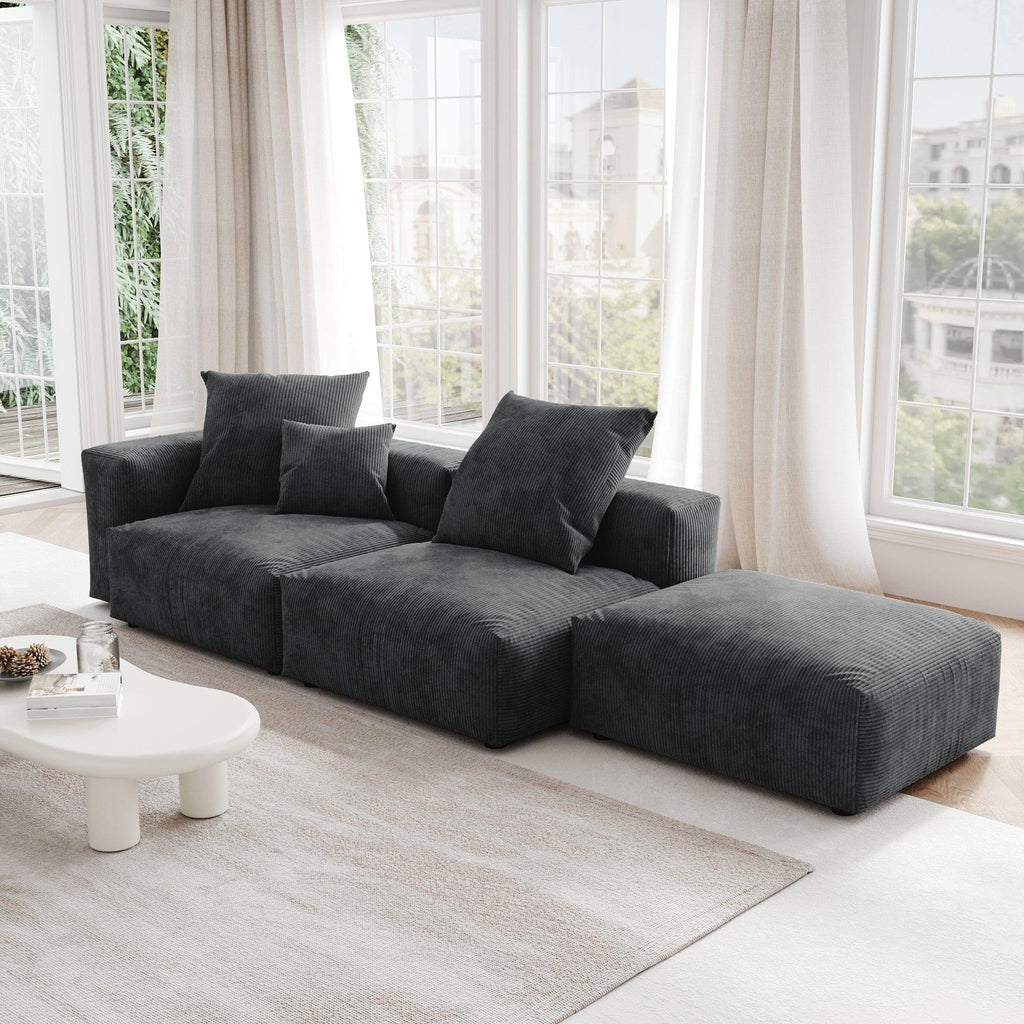 A black corduroy sectional lounger sofa with detachable armrests and removable covers, positioned in a bright room with large windows.