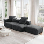 A black corduroy sectional lounger sofa with detachable armrests and removable covers, positioned in a bright room with large windows.