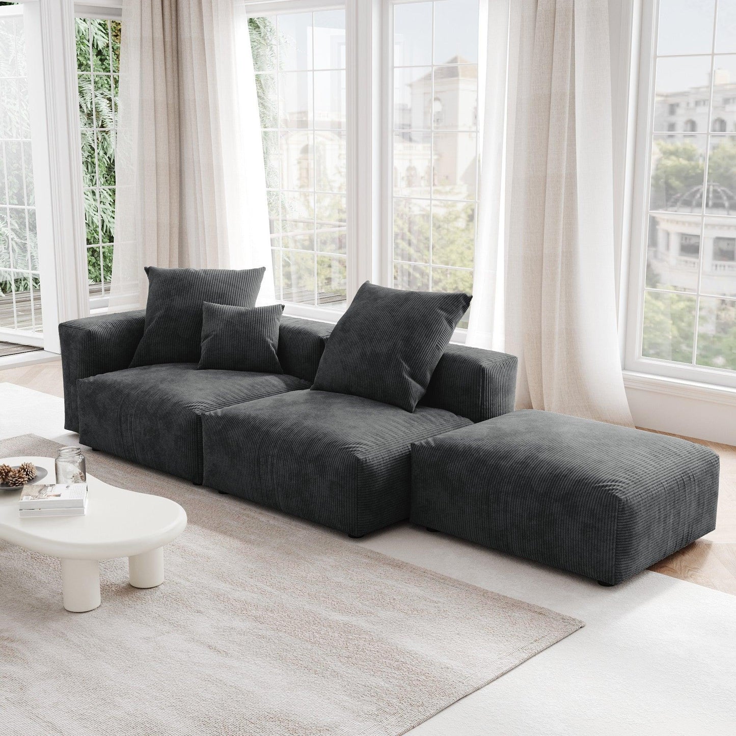 A black corduroy sectional lounger sofa with detachable armrests and removable covers, positioned in a bright room with large windows.