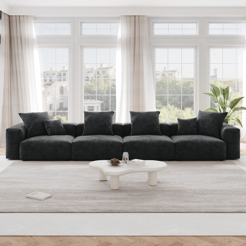 A black corduroy 4-seat sectional modular sofa with detachable armrests and removable covers, designed to seat four people, displayed in a bright room with large windows.
