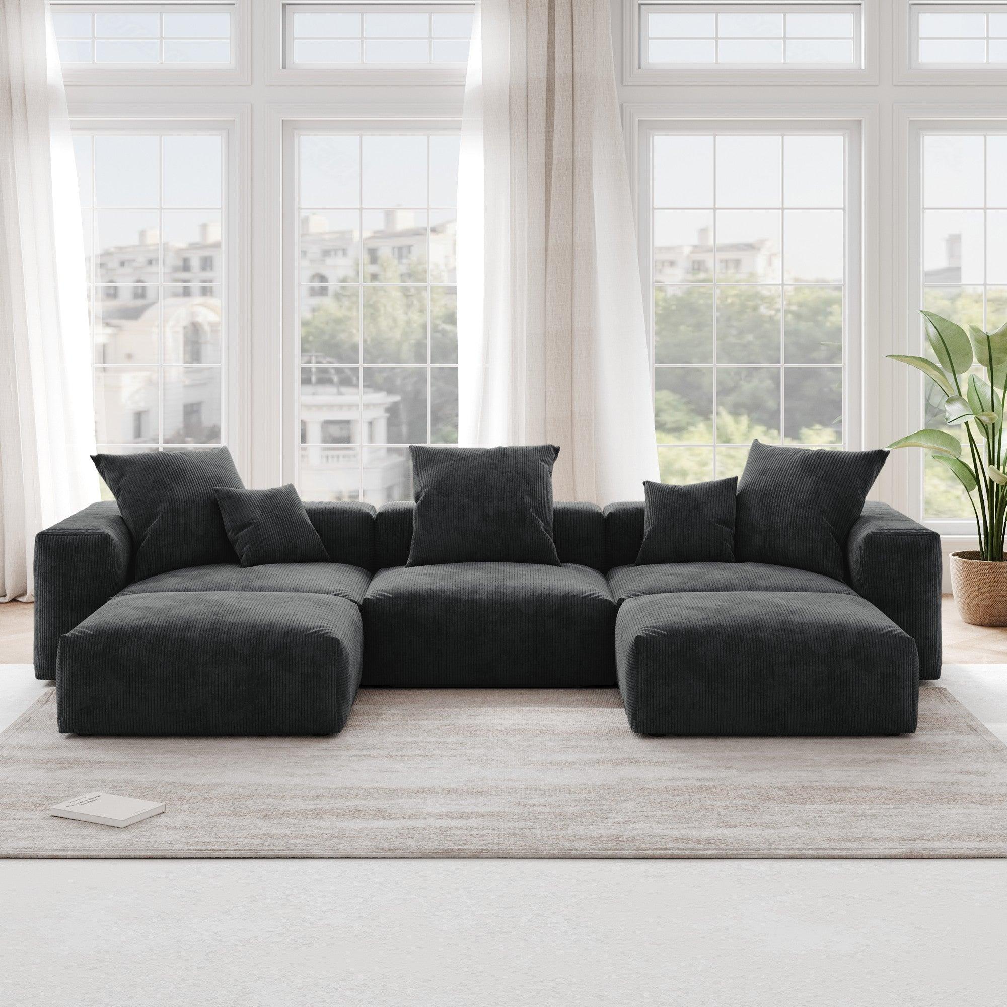 A black corduroy U-shaped sectional modular sofa with detachable armrests and removable covers, placed in a room with large windows.