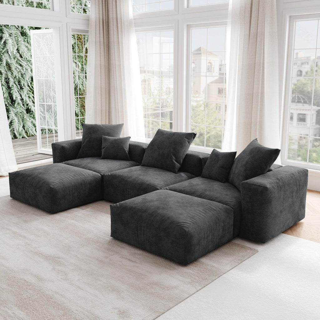 A black corduroy U-shaped sectional modular sofa with detachable armrests and removable covers, placed in a room with large windows.