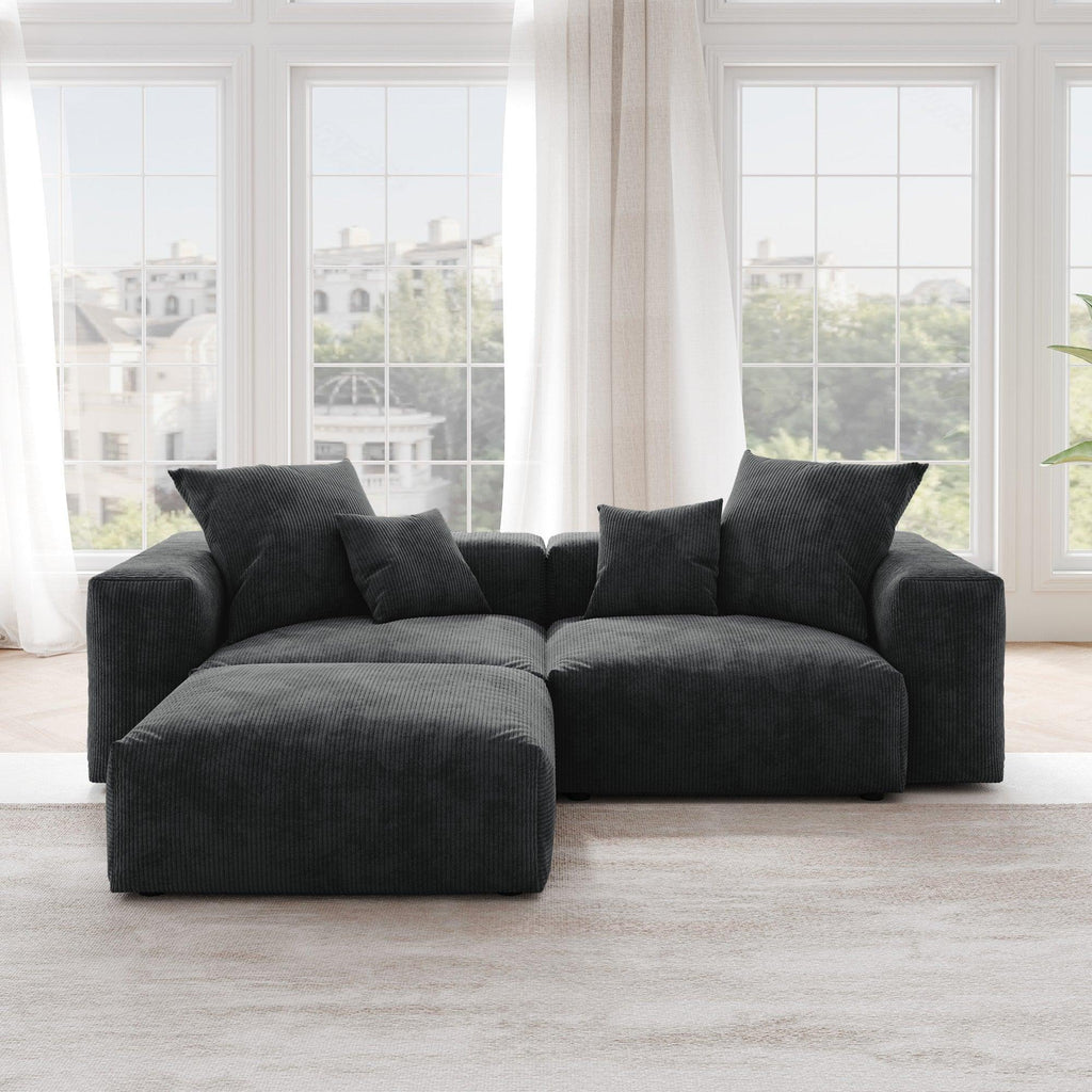 A black corduroy sectional loveseat sofa with ottoman, detachable armrests, and removable covers, featuring a chaise lounge configuration placed in a room with large windows.