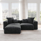 A black corduroy sectional loveseat sofa with ottoman, detachable armrests, and removable covers, featuring a chaise lounge configuration placed in a room with large windows.
