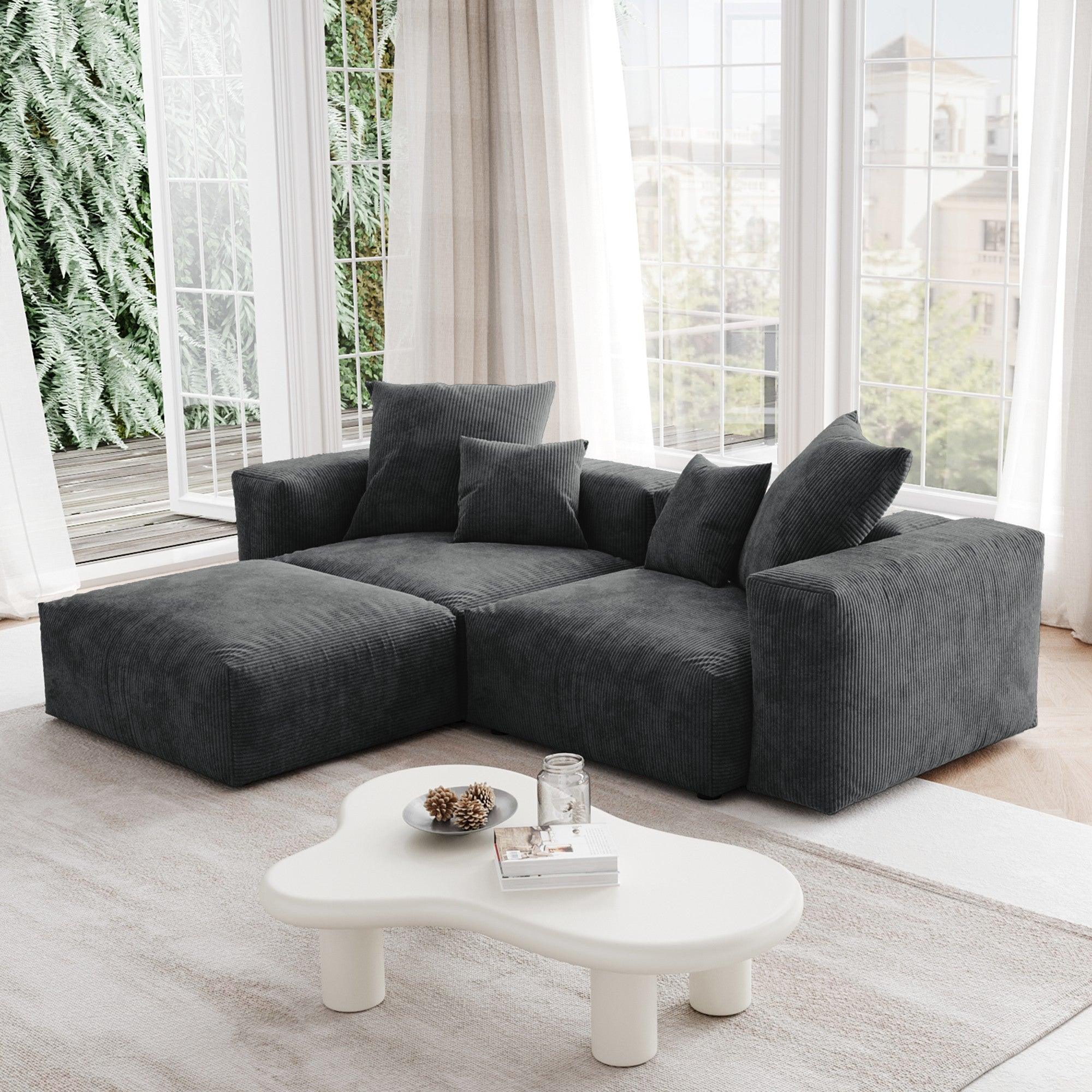 A black corduroy sectional modular sofa with detachable armrests and removable covers, featuring a chaise lounge configuration placed in a room with large windows.