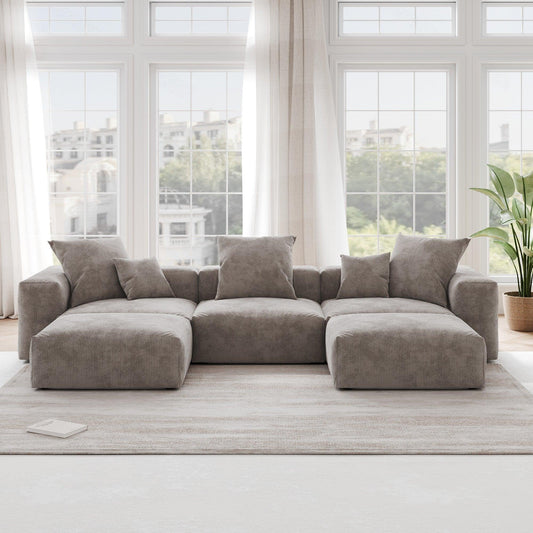 A brown corduroy U-shaped sectional modular sofa with detachable armrests and removable covers, placed in a room with large windows.