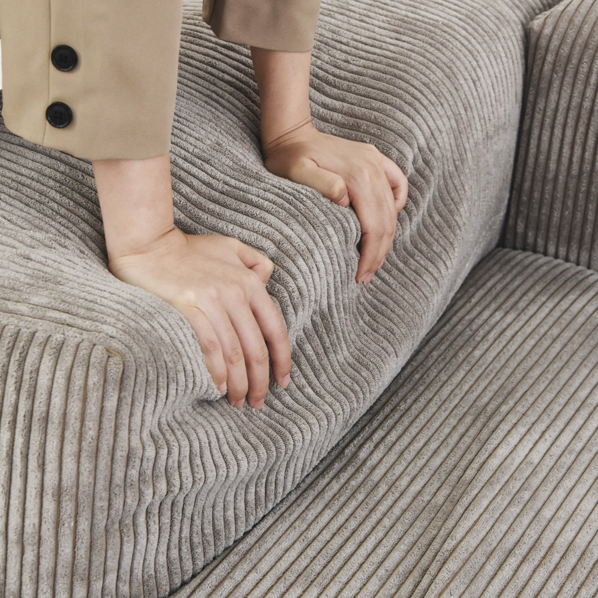 Person pressing on a backrest of a brown corduroy sofa to show its softness