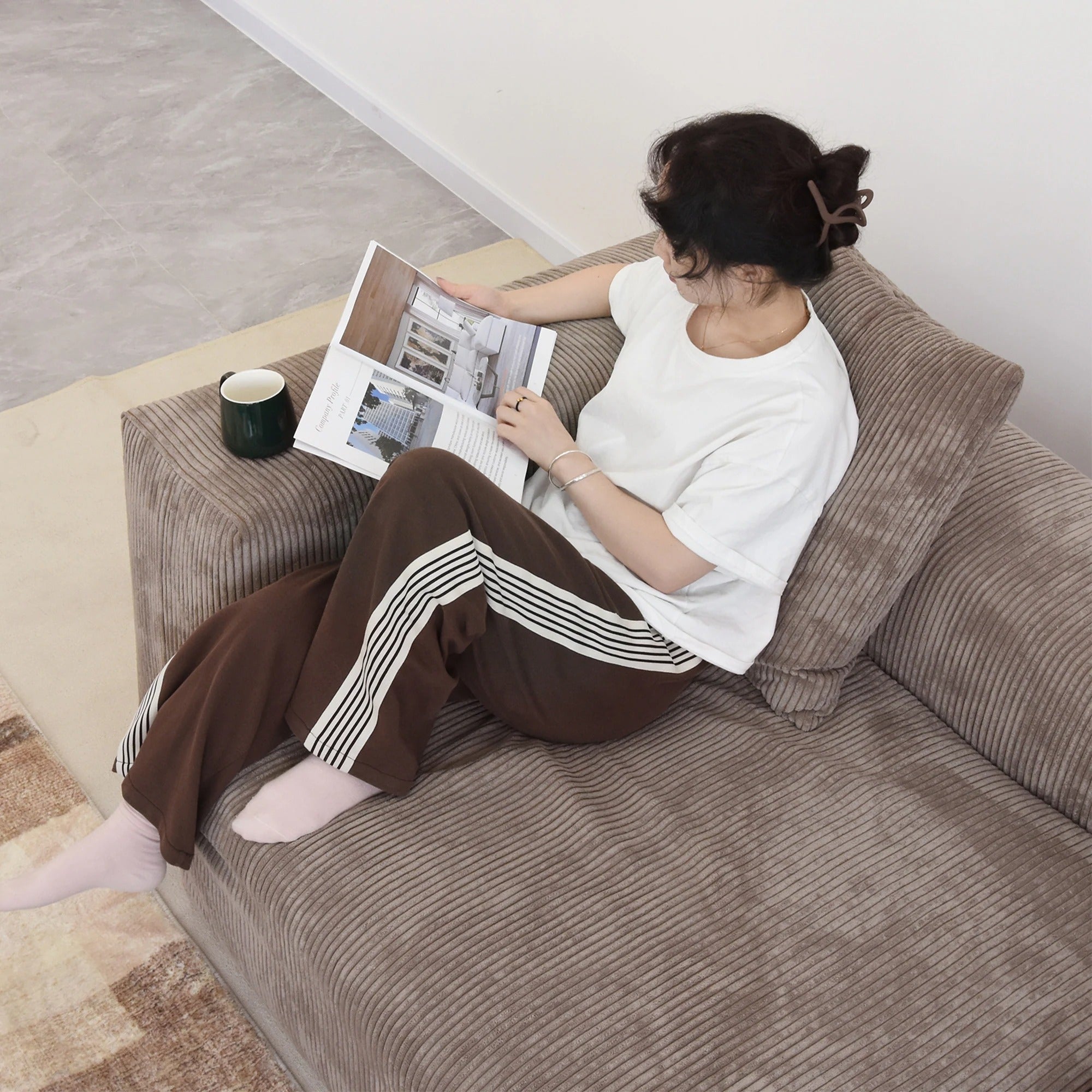 Close-up of a person sitting on a seat cushion of a brown corduroy sofa