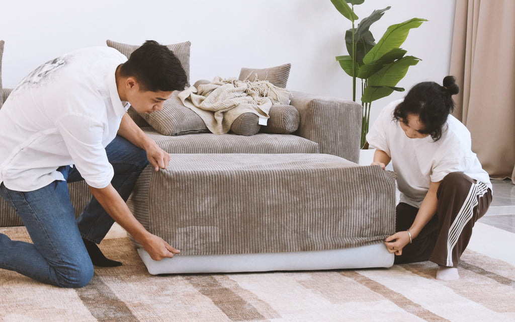 Two people putting brown corduroy cover on a sofa frame