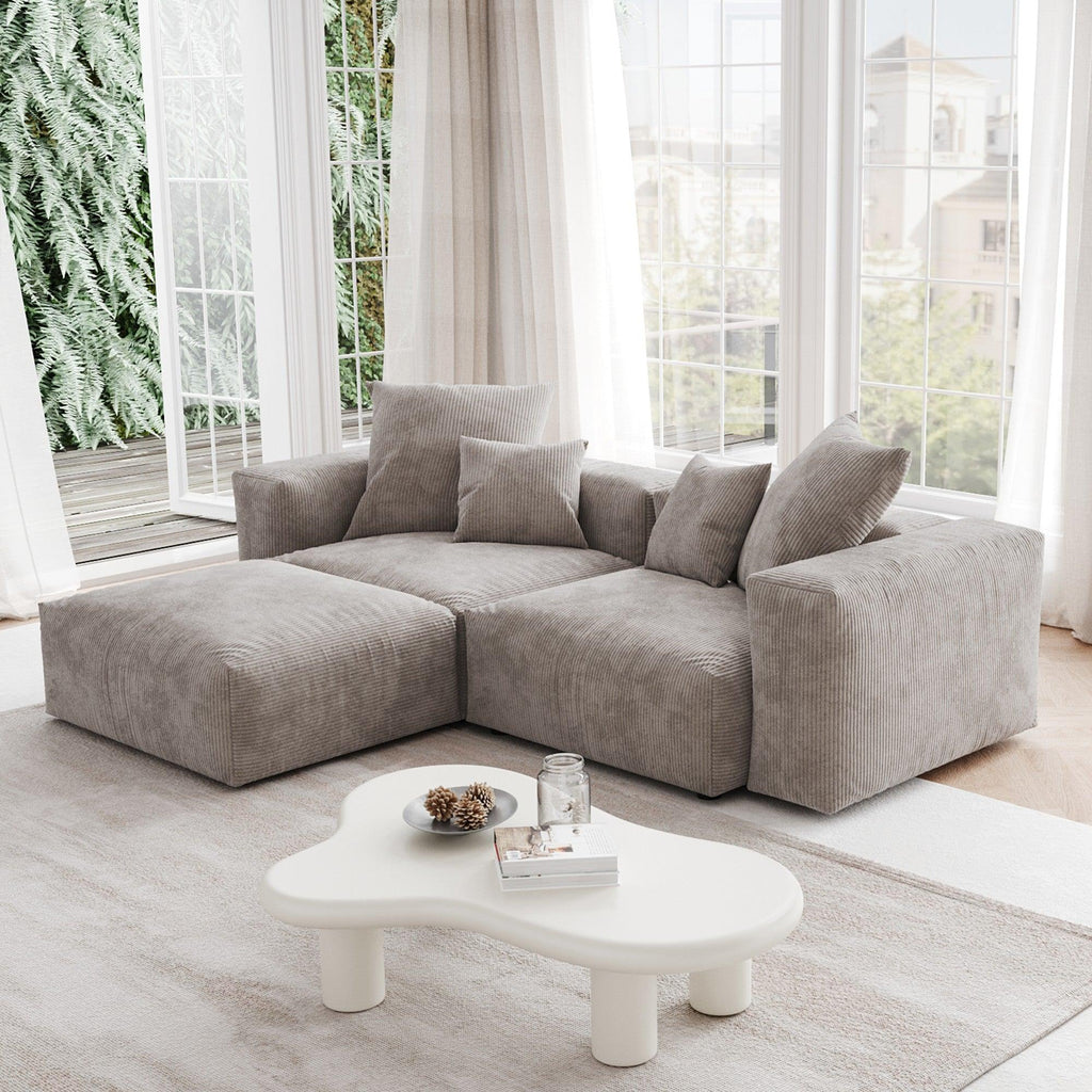 A brown corduroy sectional loveseat sofa with ottoman, detachable armrests, and removable covers, featuring a chaise lounge configuration placed in a room with large windows.