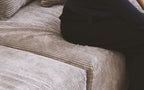 Close-up of a person sitting on a seat cushion of a brown corduroy sofa