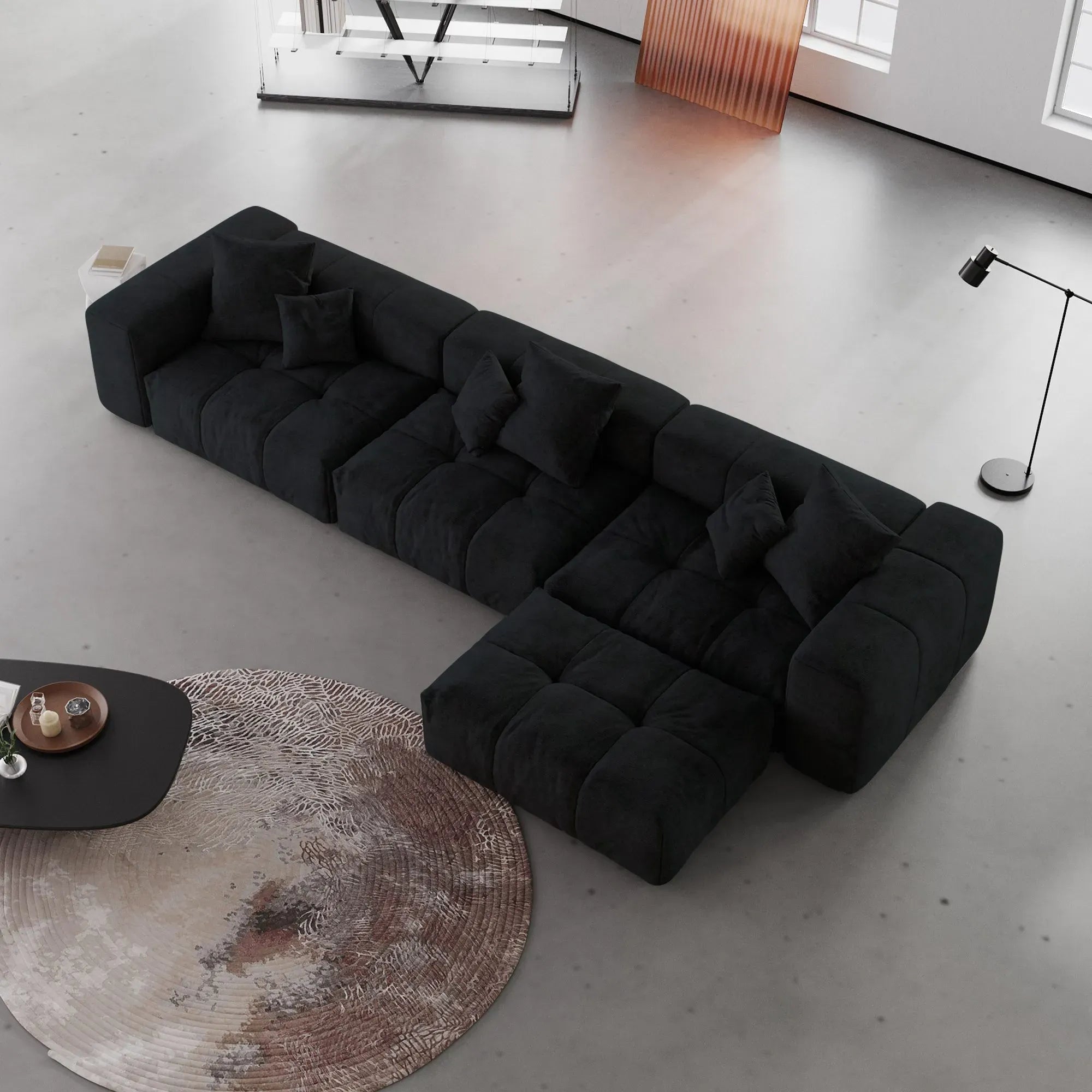 Modern black L-shaped sofa in a minimalistic living room with a round rug and coffee table.