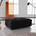 A black linen ottoman in a modern living room setting, with a low-profile and cushioned top.