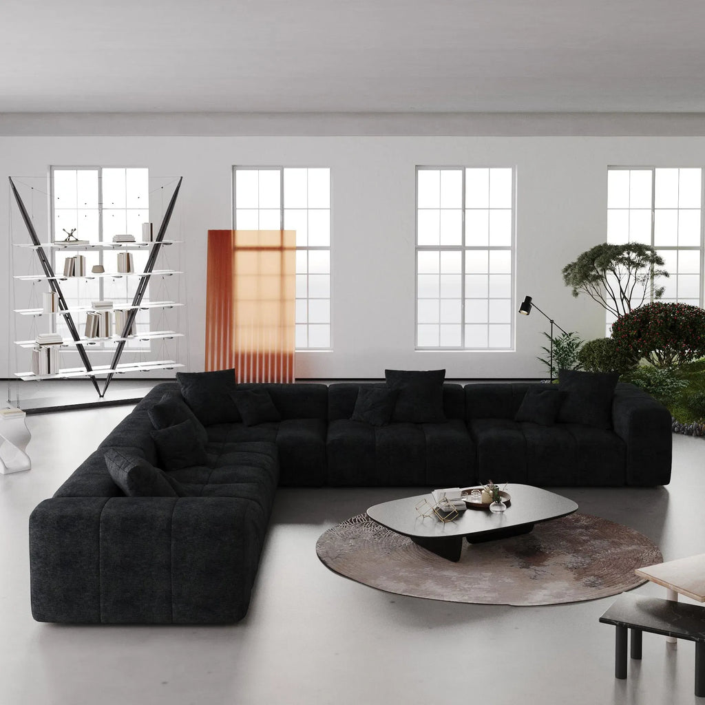 Modern living room with a black V-shaped corner sectional sofa, round coffee table, and large windows.