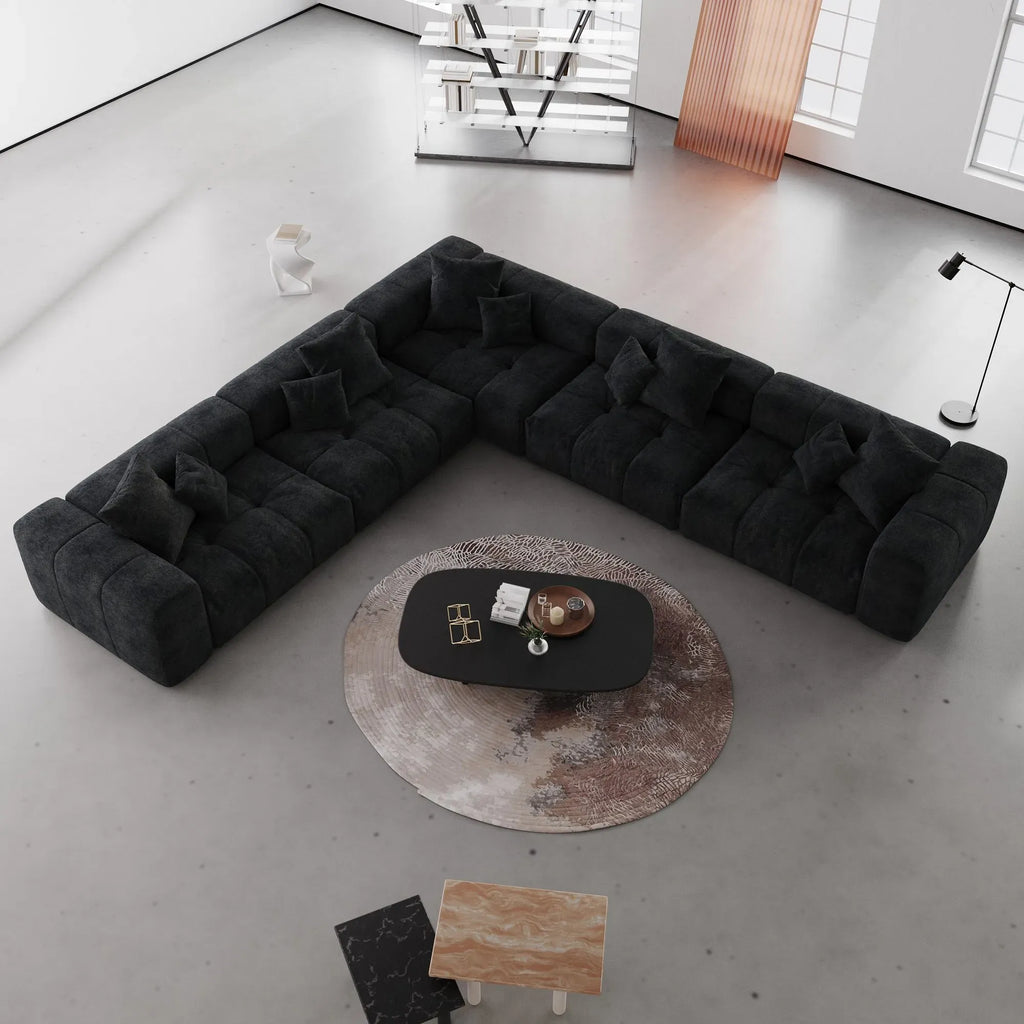 Modern black V-shaped corner sectional sofa in a minimalistic living room with a round coffee table.