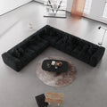 Modern black V-shaped corner sectional sofa in a minimalistic living room with a round coffee table.