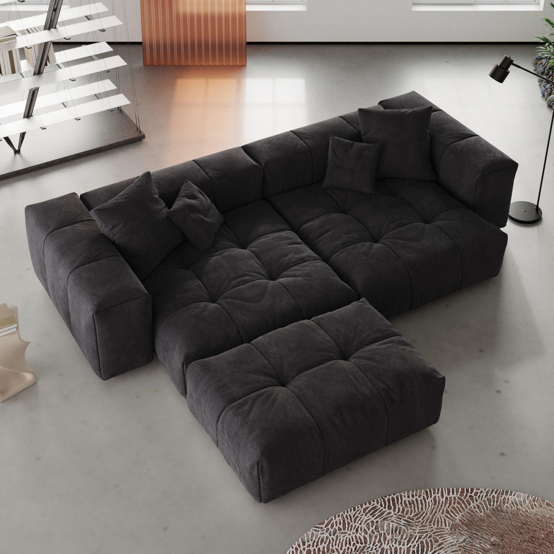 Black loveseat sofa with ottoman in a modern living room with a rug and lamp.