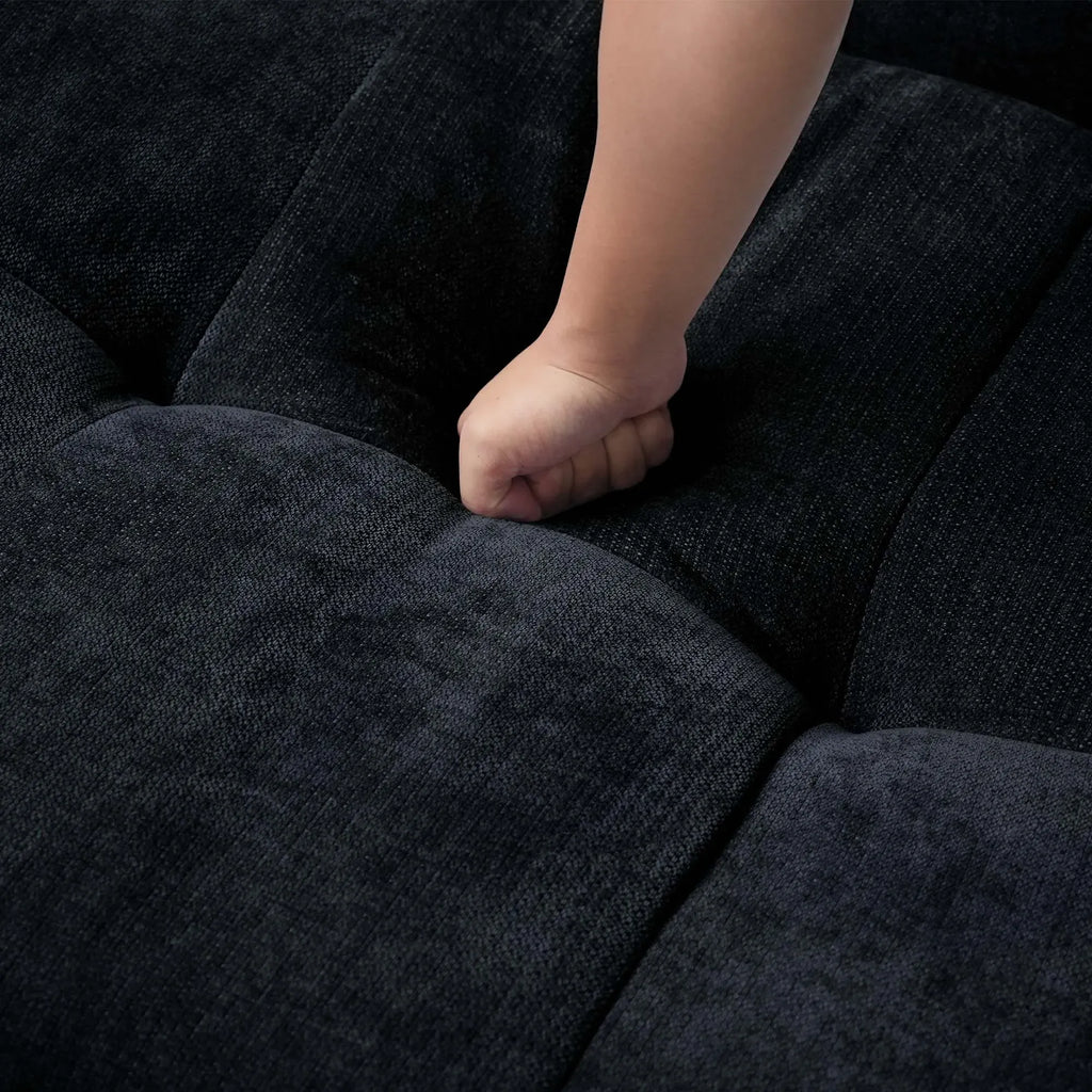 Close-up of a hand pressing on a seat cushion of a black sofa