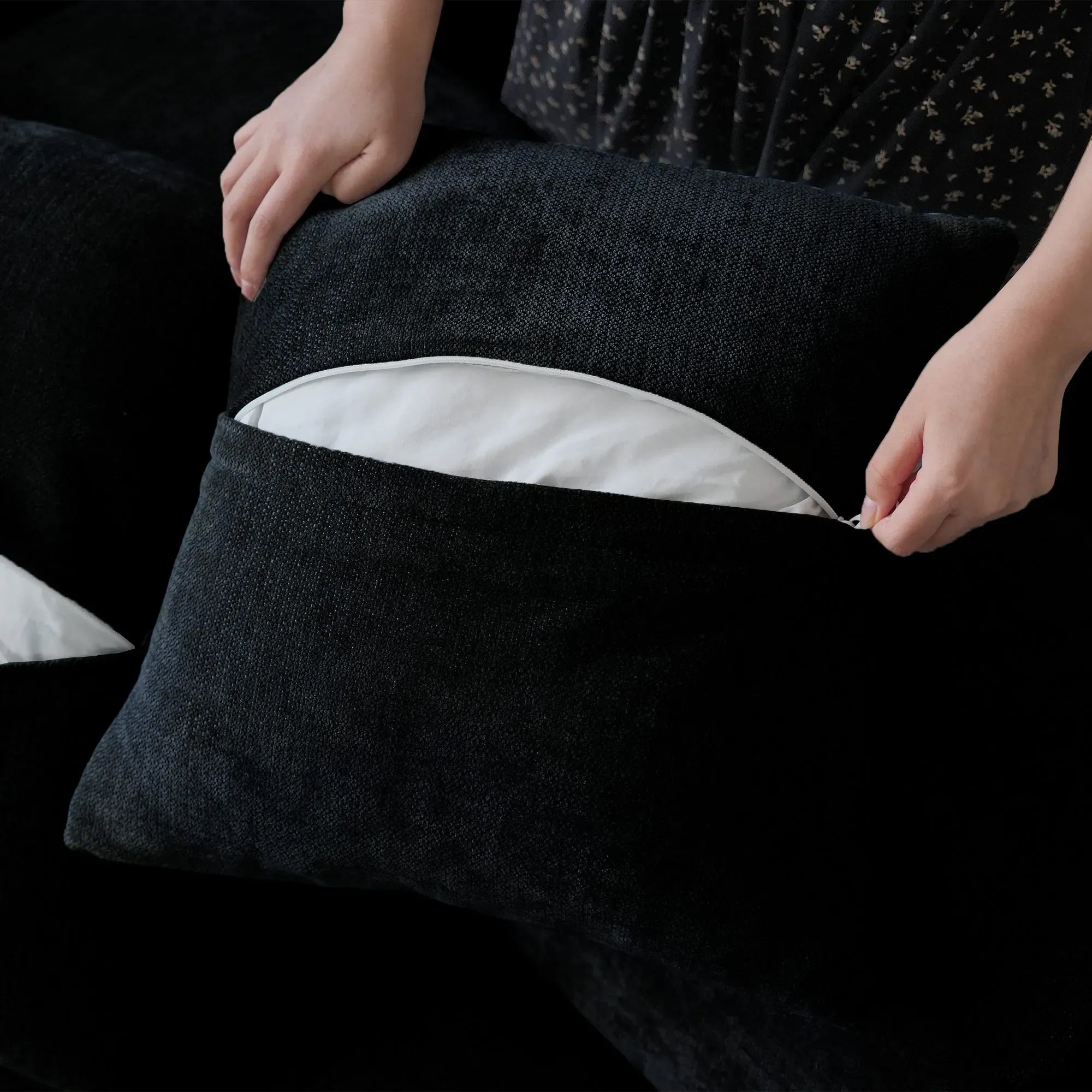 Person unzipping a pillow cover of a black sofa