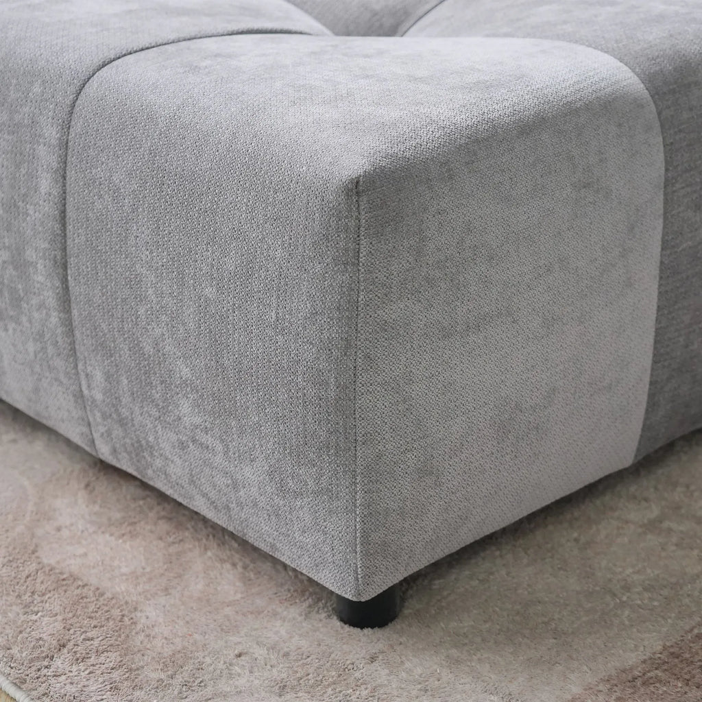 Gray upholstered corner of a seat of a gray sofa on a carpeted floor