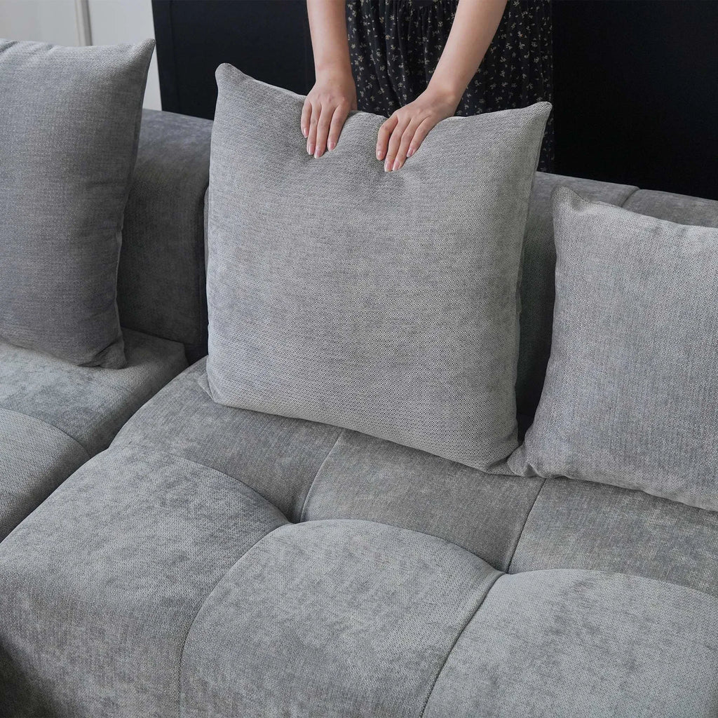 Person adjusting a gray pillow on a gray sofa