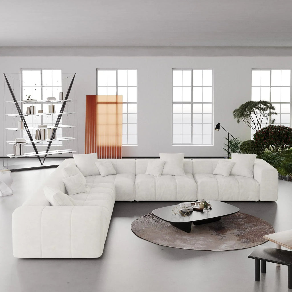 Modern living room with a large white V-shaped corner sectional sofa, coffee table, and decorative elements.