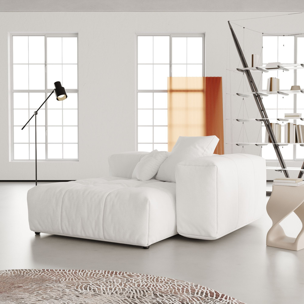 Modern white modular seat in a minimalistic living room with a bookshelf and lamp.