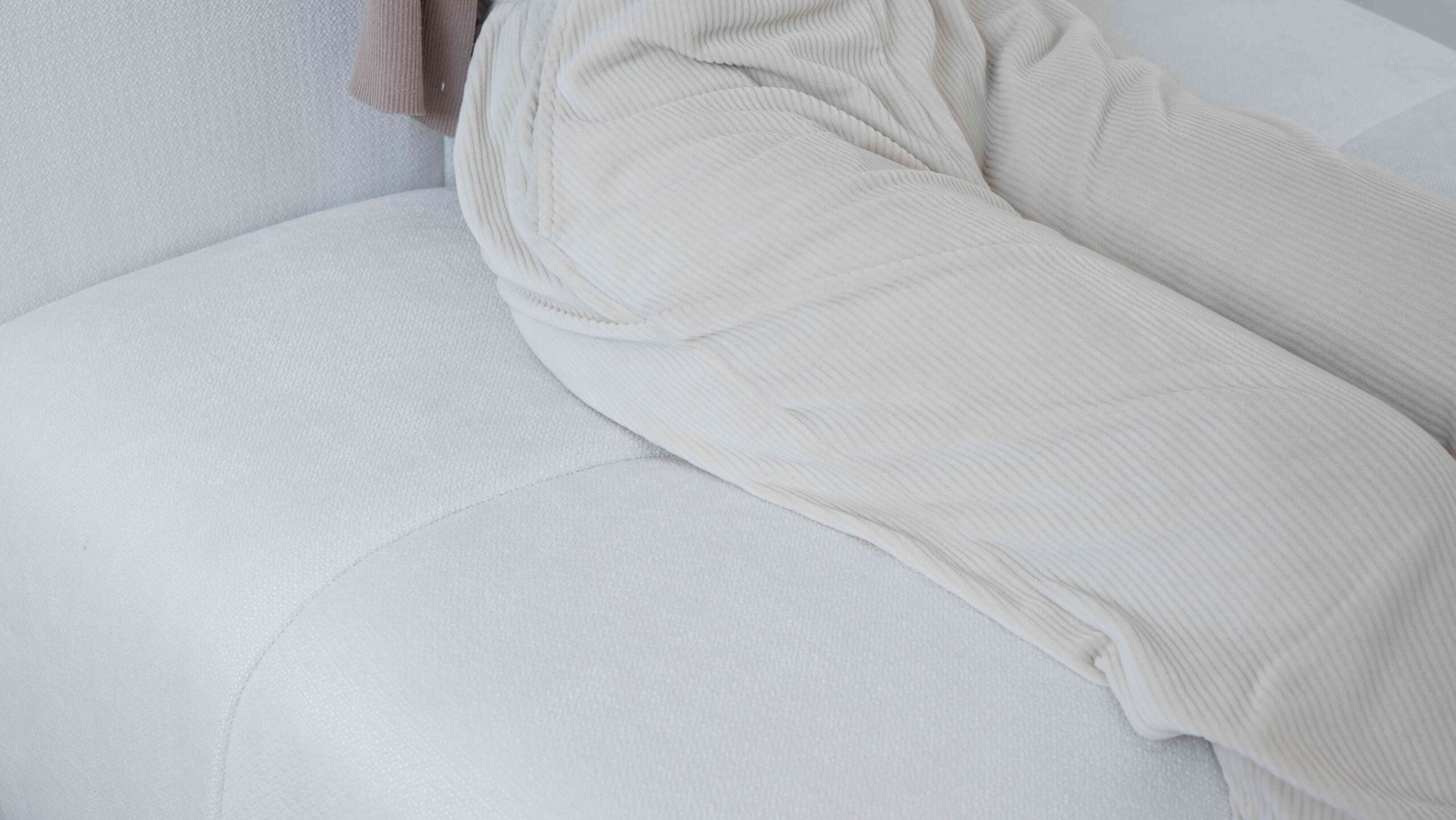 A close-up of a person sitting on the a white sofa, showcasing its comfort
