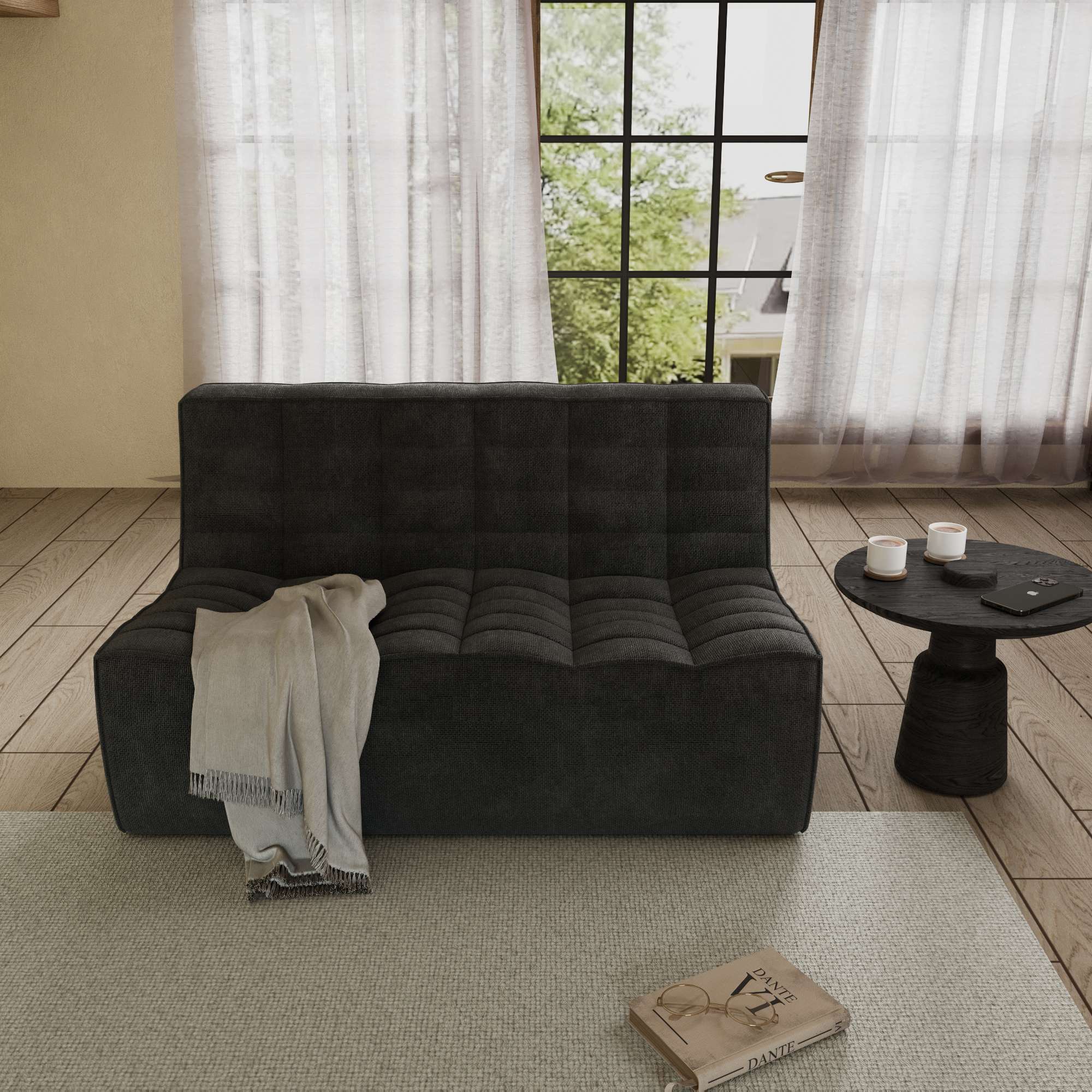 A black Floor Chenille Sofa with an ergonomic caterpillar design, placed in a room with a window, curtains, a small round table, and a book on the floor.