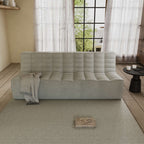 A beige chenille sofa with a minimalist design, placed in a room with a window, curtains, and a small round table with an object on it.