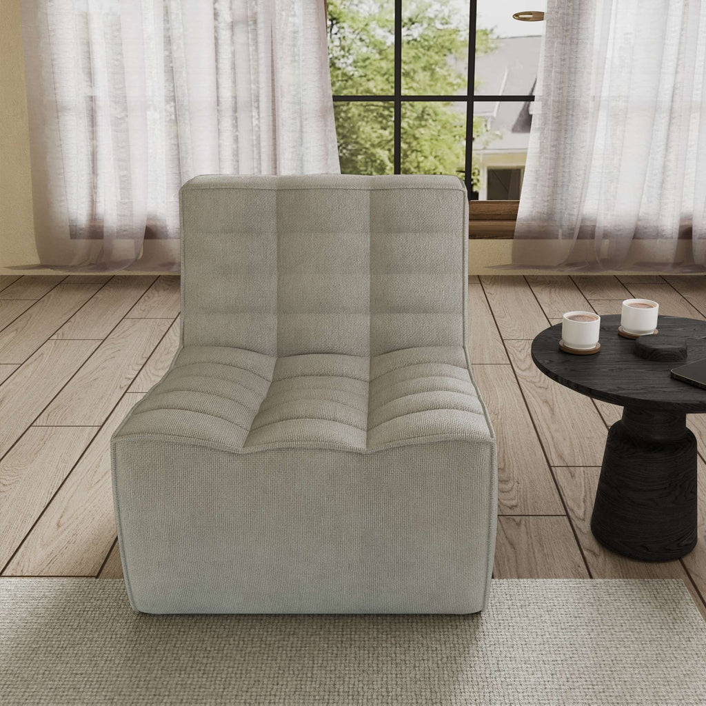 A light gray chenille accent chair with a minimalist design, positioned in a room with a window, curtains, and a small round side table.