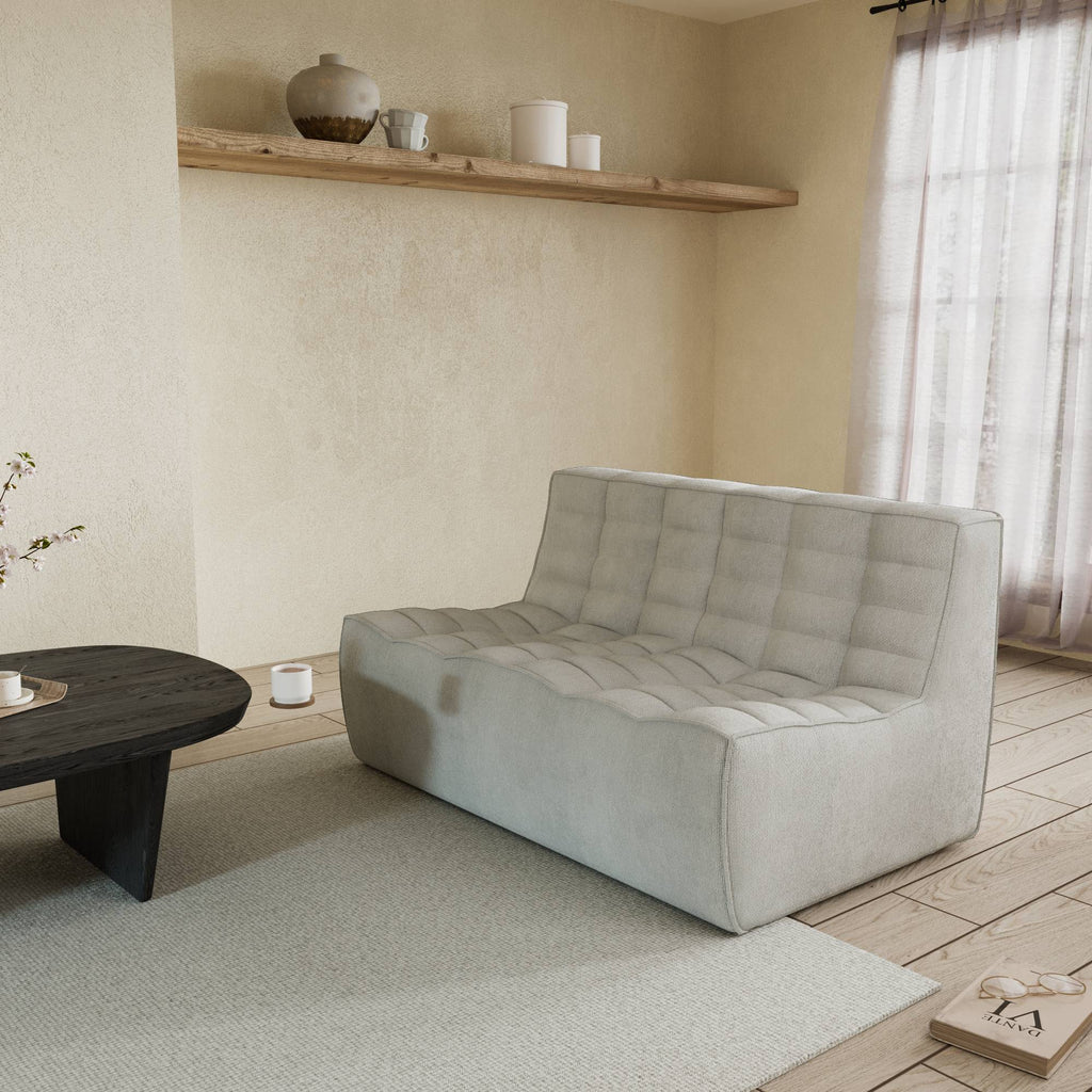 A light gray cotton-linen 2-seater sofa with an ergonomic caterpillar design, placed in a room with a window, curtains, a small round table, and a book on the floor.