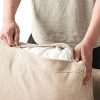 Person unzipping a linen cover of a backrest cushion of a khaki couch