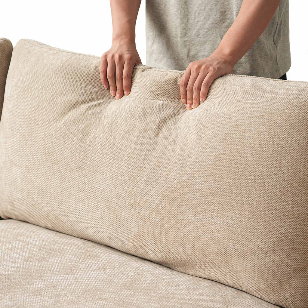 Person squishing a backrest cushion of a khaki sofa to show its softness