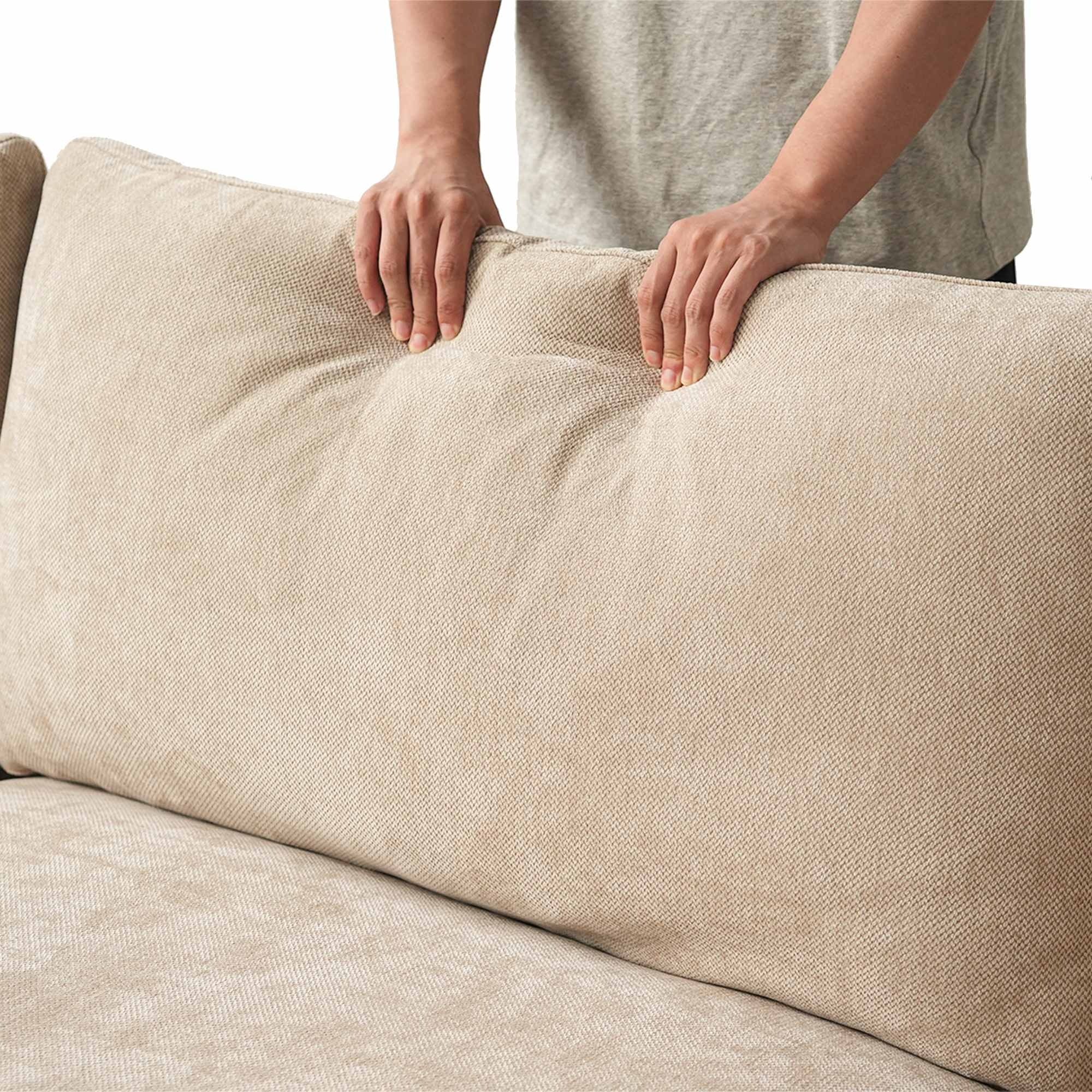 Person squishing a backrest cushion of a khaki sofa to show its softness