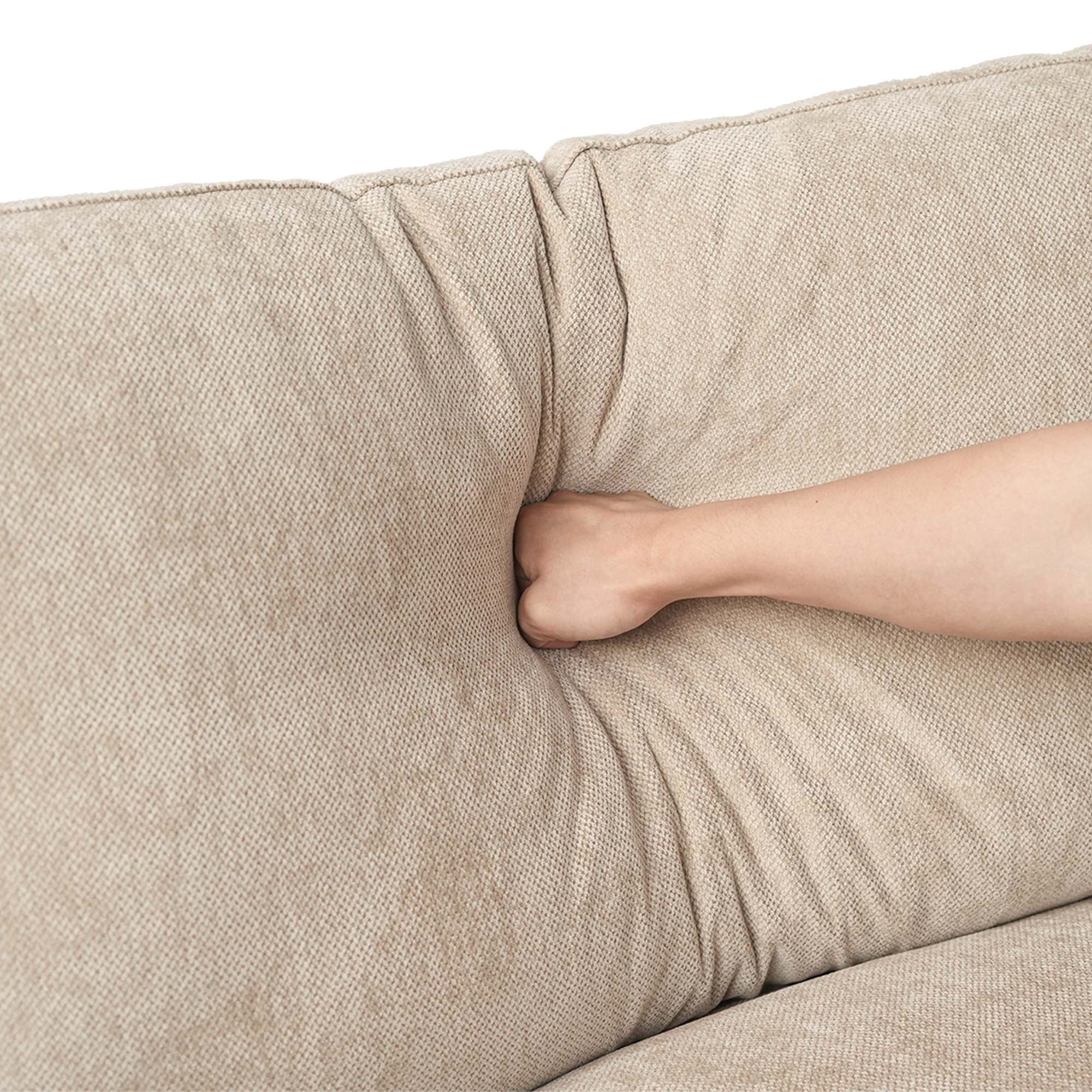 Close-up of a hand pressing on a backrest cushion of a khaki sofa